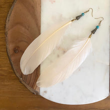 Load image into Gallery viewer, Close-up of Fauna cruelty free feather earrings made from ethically sourced goose feathers in a beautiful champagne peach color. Each earring features a brass cone cap with a wave design, an impression jasper bead, and raw brass French hook ear wire.

