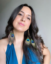 Load image into Gallery viewer, Woman wearing a Fauna eucalyptus and organic cotton maxi dress and cruelty free feather earrings made from gorgeous ethically sourced peacock feathers. Each earring features 2 peacock feathers, brass chain, raw brass fold over clasps, o-rings, and french hook ear wires.
